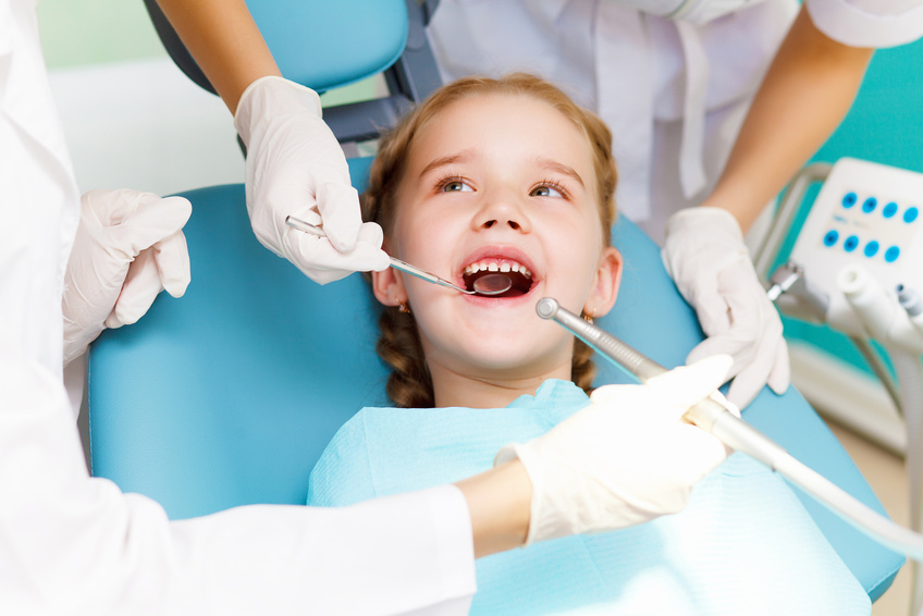 Family Dental Clinic - A young child in a dental chair, looking up and smiling while getting dental treatment